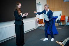 En mand i jakkesæt udfører et trick for en kvinde på en scene.