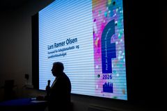 "En mand står foran en skærm med tekst og farver i baggrunden."