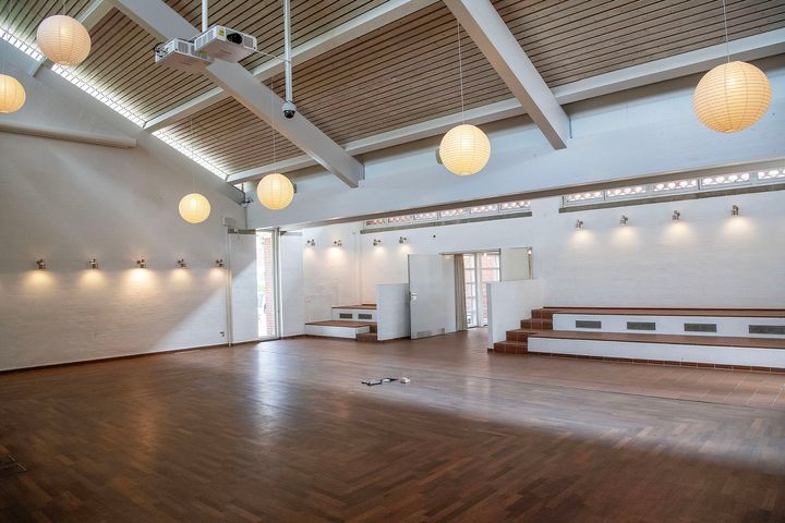 Lys og renoveret mødesal med træloft og kuglelamper.