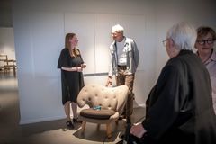 En gruppe mennesker står ved siden af en ompolstret stol i et udstillingsrum.