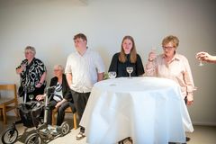 En gruppe mennesker, inklusiv to unge, står ved et bord med glas på Museum Wegner i Tønder til fejring af medaljevindere fra DM i Skills.