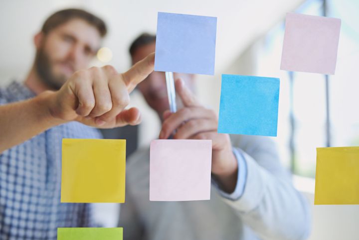 To personer placerer farverige post-its på en glasvæg.