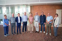Bestyrelsen for Uddannelse Tønder står sammen i et moderne kontorlokale med en murstensvæg i baggrunden.