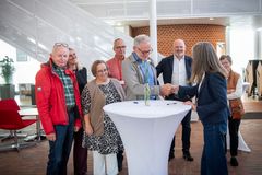 Gruppe af mennesker står sammen indendørs ved et bord, mens to personer giver hinanden hånden.
