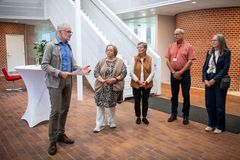Fem mennesker står sammen indendørs, mens en person holder en tale.