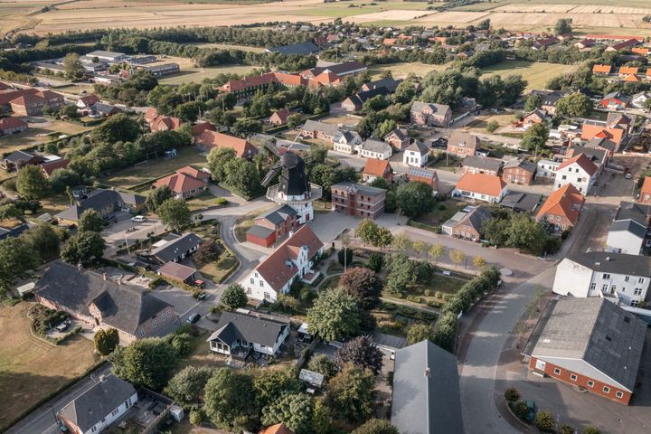 Luftfoto af en Højer med røde tegltage, grønne områder og omkringliggende marker.
