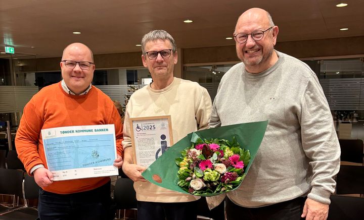 Tre personer poserer med Handicapprisen 2025 og en buket blomster.