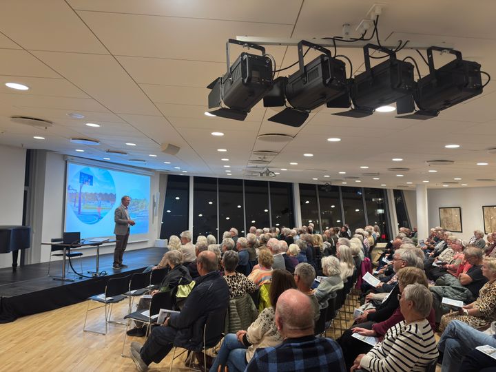 Billede af en foredragsholder på en scene foran et publikum til et borgermøde om seniorboliger.