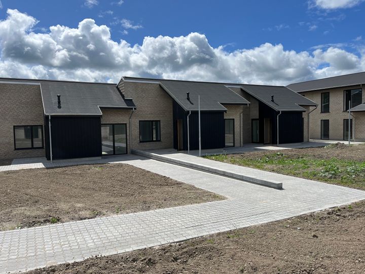 Nybyggede rækkehuse med grå tagsten og murede facader under en blå himmel med skyer.