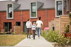 To personer går ved siden af en person på cykel foran en moderne boligbygning med røde facader.
