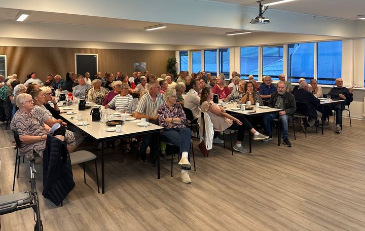 En stor gruppe beboere sidder ved borde til et informationsmøde i et lyst lokale.