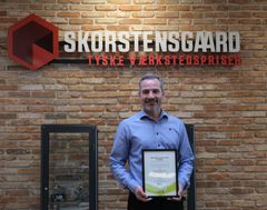 Anders Skorstengaard står med SammenomJOB-prisen på kontoret i Skorstensgaards hovedkvarter.