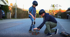 En far hjælper sin søn med at lære at stå på skateboard – en aktiv, fælles og meningsfuld aktivitet, der fremmer børns trivsel og sundhed - en evidensbaseret tilgang kaldet 'ABC for mental sundhed'. Metoden ligger til grund for Dansk Sundhedssikring to gratis pjecer med gode råd til forældre, så de kan støtte børn til trivsel.