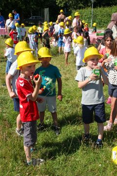 Børn med gule byggehatte nyder frugtspyd på en udendørs event.