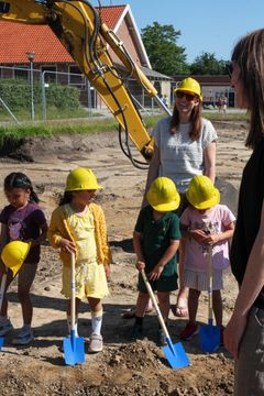 Børn graver på byggeplads med gravemaskine i baggrunden-