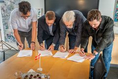 Fire mænd underskriver hver deres eksemplar af et papir, imens de står for enden af et bord