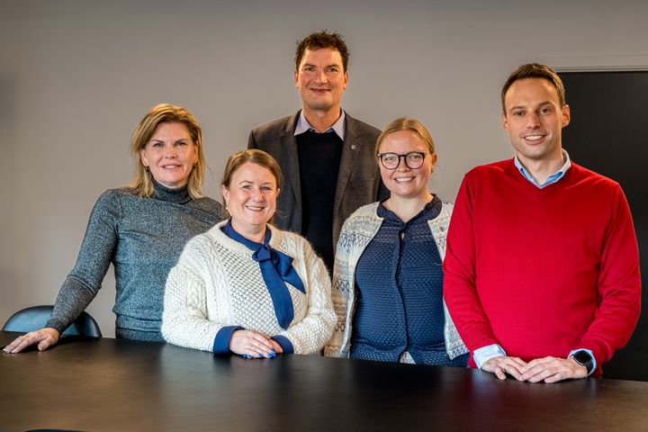 Fem personer står ved et bord.