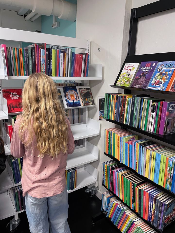 En person med langt blondt hår kigger på bøger i en bogbutik.