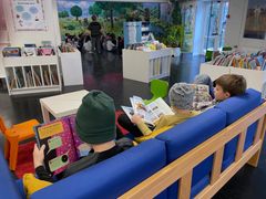 Tre drenge læser bøger i sofaen på et bibliotek.