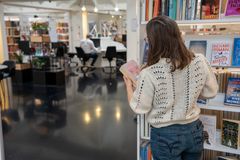 En person læser en bog blandt hylder i et moderne bibliotek med mødefaciliteter i baggrunden.