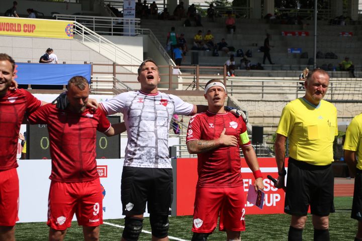 Danske fodboldspillere i røde dragter står på række og synger nationalmelodien ved Homeless World Cup i Seoul 2024.