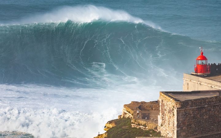 Giant wave outside Nazare, Portugal, crashing into cliff and lighthouse after major Atantic Storm. Photo: Getty