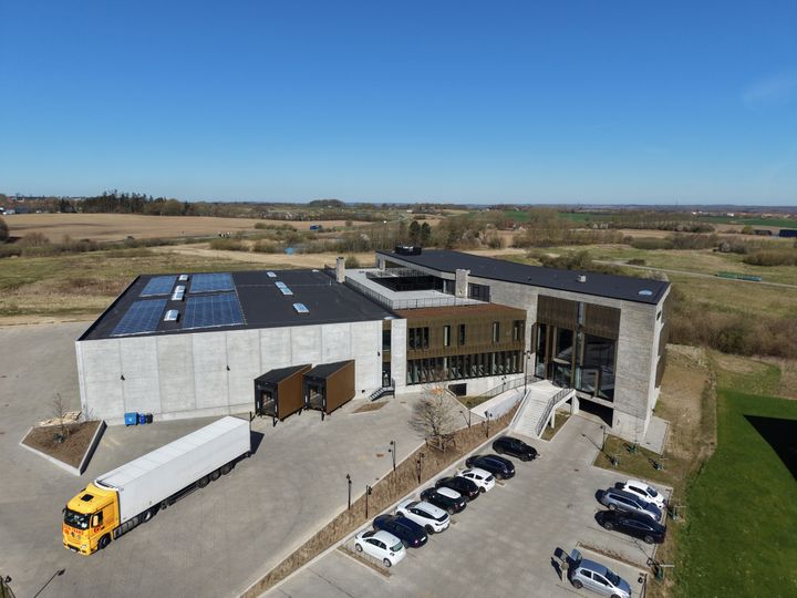 Luftfoto af modernistisk kontorbygning med solpaneler på taget og parkeringspladser foran.