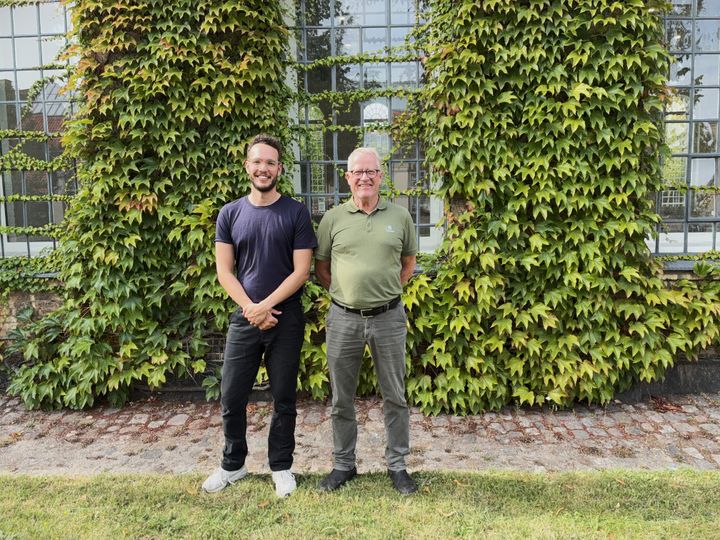 To personer står foran en mur dækket af planter.