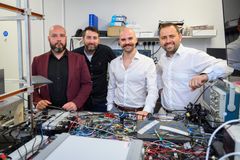 CEO Andrei Dragomir, CSO Matt Himsworth, kvanteingeniør Chester Camm og COO Alexander Jantzen står sammen i et teknologilaboratorie.