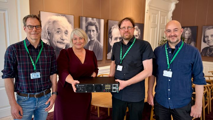 Forsknings-, Uddannelses- og Digitaliseringsminister Christina Egelund og lederen af QCI-projektet Tobias Gehring, DTU, med systemet til fordeling af kvantenøgler, QKD systemet.  I løbet af projektet har Tobias Gehring sammen med Ulrik Lund Andersen, professor på DTU (længst til venstre) og Asger Trier Bing (længst til højre) startet en spinout virksomhed, Celare Quantum Communications, der skal kommercialisere den teknologi, der anvendes i det nye kvantenetværk. Foto: Uffe Frandsen