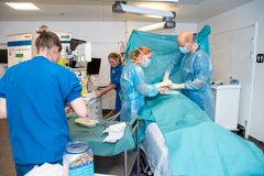 På billedet ses et operationshold der står ved operationsbordet og er i gang med at operere en patient, der dog i dette tilfælde er en dukke, da der er tale om simulationstræning.