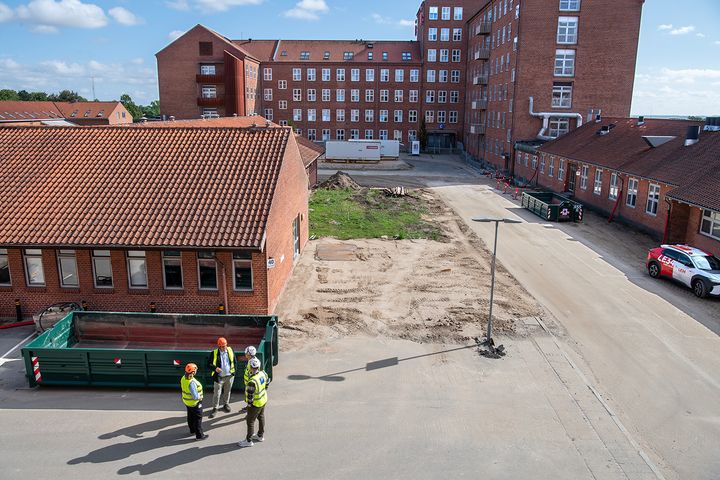Billedet viser et overblik over byggepladsen, hvor Vita-byggeriet skal foregå. På billedet ses også fire personer i gule veste.