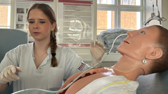 En anden af folkeskoleeleverne, prøver kræfter med at lægge en ernæringssonde på en dukke.