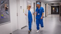 To sundhedspersoner i kittel i samtale på en hospitalsgang.