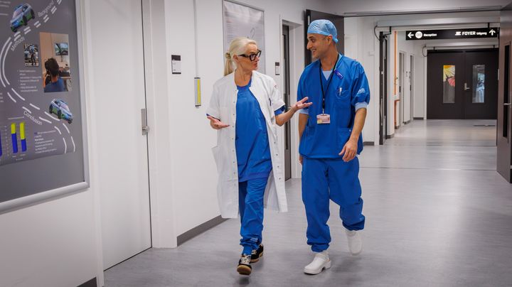 To sundhedspersoner i kittel i samtale på en hospitalsgang.
