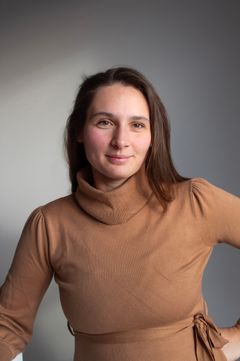 Kvinde i brun trøje foran grå baggrund.