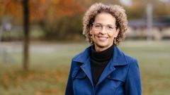 KVinde i blåt og sort tøj med grøn natur i baggrunden.