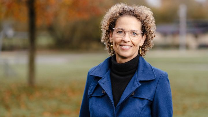 KVinde i blåt og sort tøj med grøn natur i baggrunden.