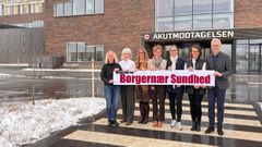 En gruppe mennesker står foran en bygning med et skilt for "Borgernær Sundhed".