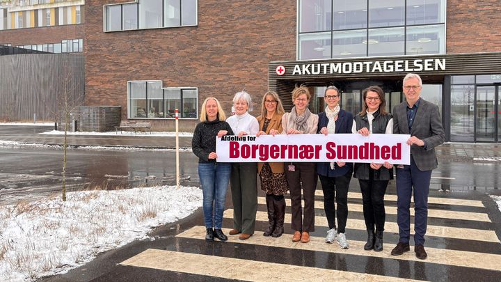 En gruppe mennesker står foran en bygning med et skilt for "Borgernær Sundhed".