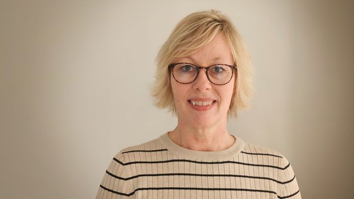 Portræt af kvinde  med briller iklædt i hvid bluse med striber på lys baggrund.