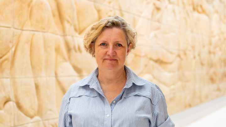 Kvinde i lys bluse med lyst kunstværk i baggrunden.