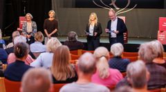 Fire personer står på en scene foran et siddende publikum.