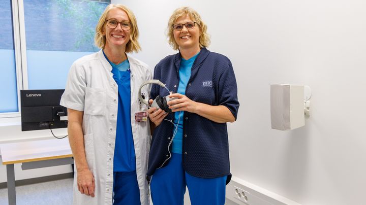 Smilende kvinde i lægekittel og smilende kvinde i blå hospitalsuniform i en ny høreklinik i Gødstrup.