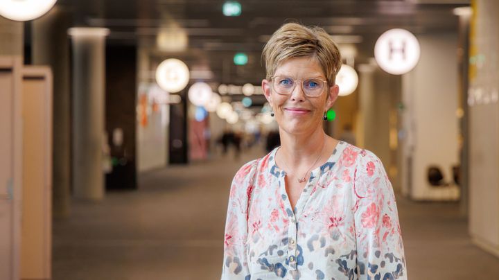 Portræt af smilende kvinde med briller i et hospitalsmiljø.