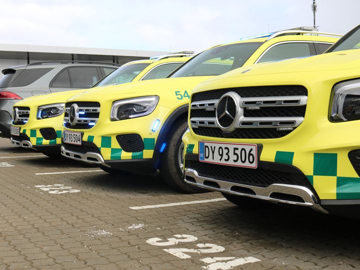 Flere parkerede gule sygebesøgsbiler med blåternede markeringer.