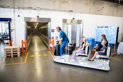Mor og to børn køres ind i elevator i et hospitalskøretøj af medarbejder klædt i blåt hospitalstøj.