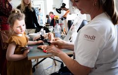 Kvinder i hvidt hospitalstøj viser en fingerprotese, mens en lille pige kigger nysgerrigt på.