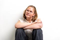 Ung pige med briller og lyst hår sidder afslappet med armene rundt om knæene og kigger ud til venstre.