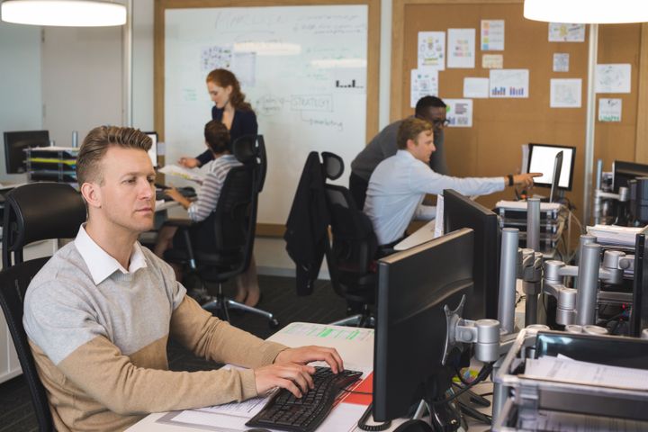 Mand skriver på computer med kolleger i baggrunden